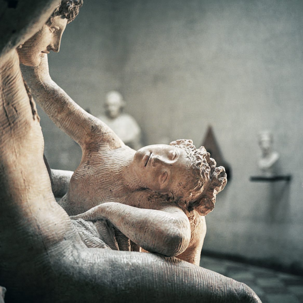 Marble sculpture of embracing couple in a museum setting with natural light and a blurred background. Focus on classical art.