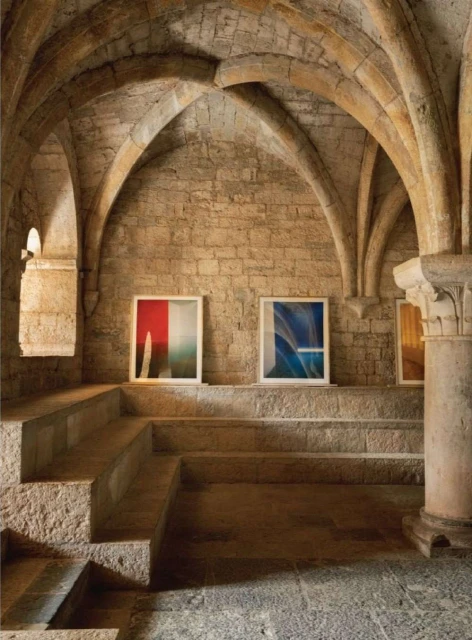 Arched stone staircase in a medieval-style interior with abstract art pieces displayed on the landing, creating a serene, gallery-like atmosphere.