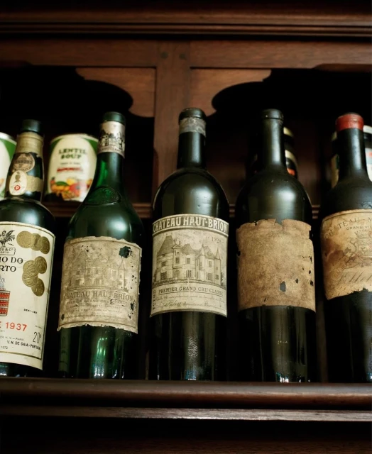 A collection of vintage wine bottles with aged labels are displayed on a dark wooden shelf, showcasing their unique character and history.
