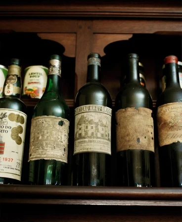 A collection of vintage wine bottles with aged labels are displayed on a dark wooden shelf, showcasing their unique character and history.
