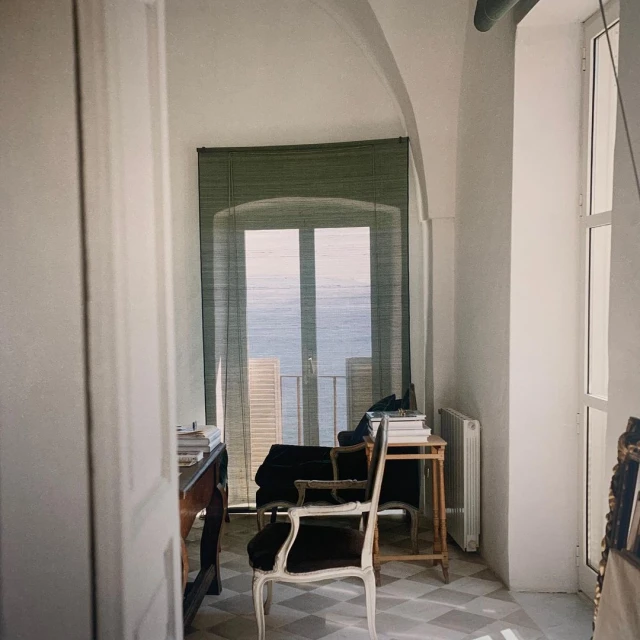 Sunlit room with sea view features a desk, chair, radiator, and tiled floor, creating a serene, inviting workspace.