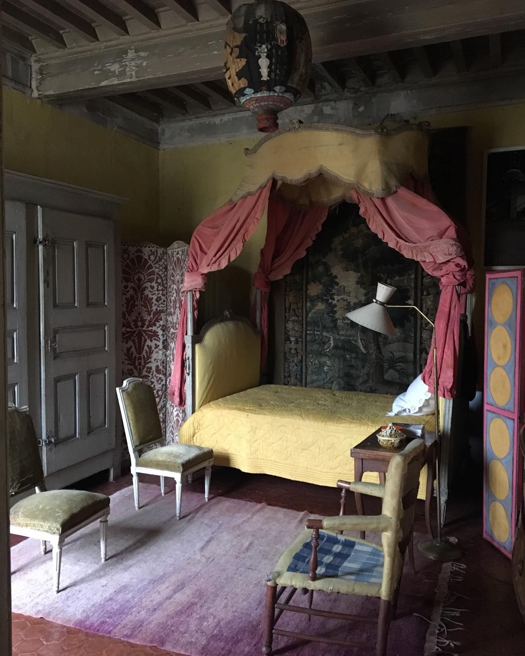Ornate bedroom interior with a yellow four-poster bed, antique furniture, vintage decor, and a purple rug in a historic house.