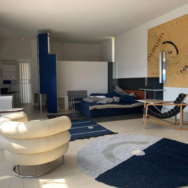 Modern interior with a blue sofa, black lounge chair, and cream-colored chair, lit by natural light. Minimalist furniture and decor in a spacious room.