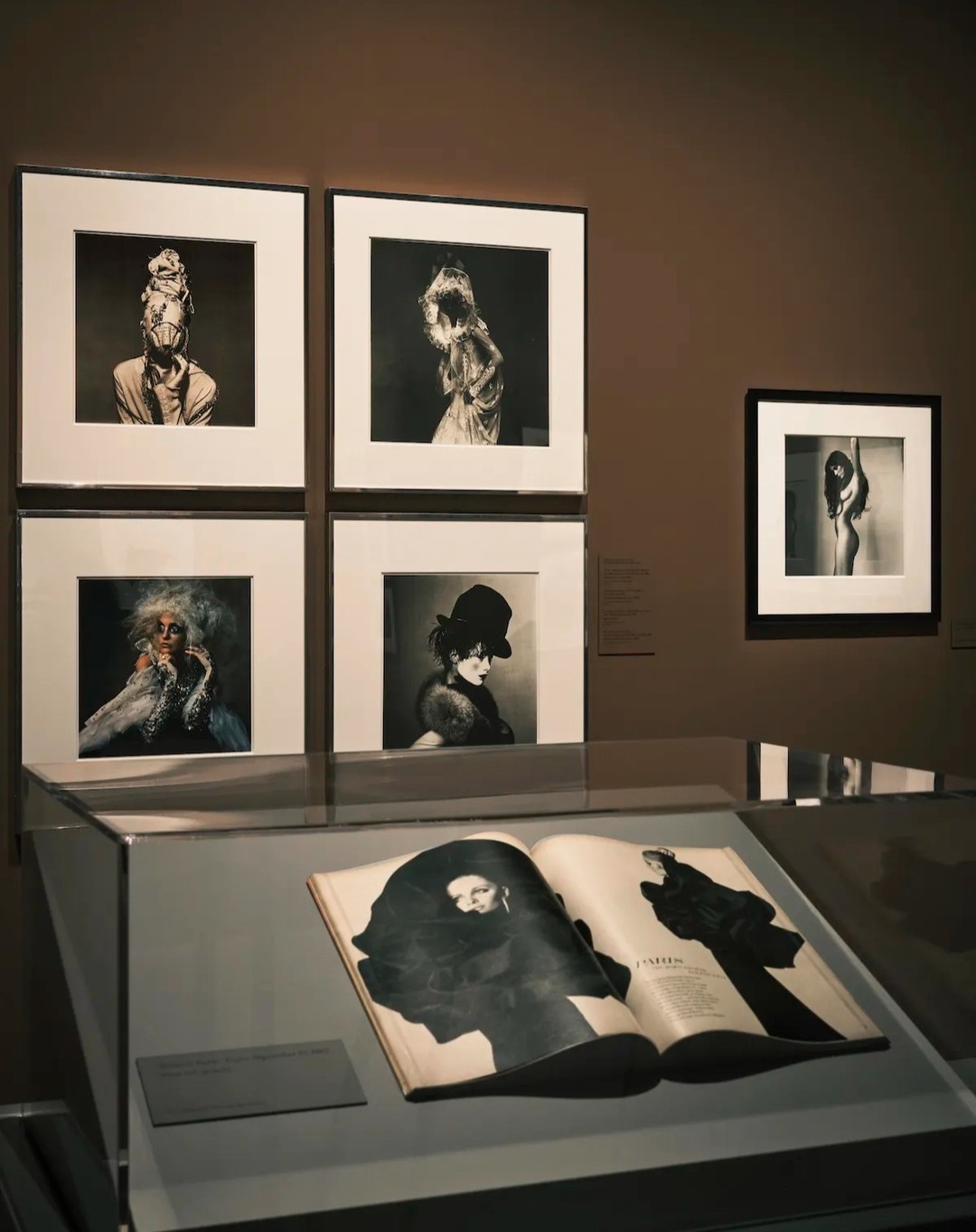 Display of framed black and white photographs and an open magazine in a museum exhibit, showcasing portrait and figure photography.