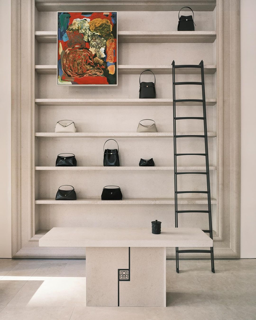 Display of handbags on shelves with painting and ladder in minimalist setting, highlighting fashion and interior design elements.