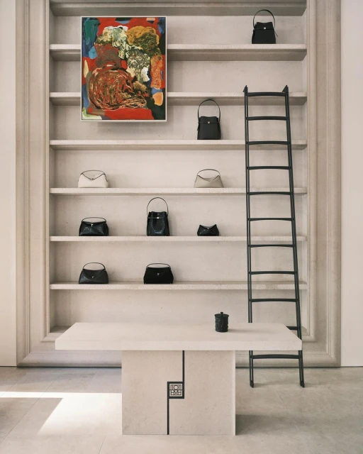 Display of handbags on shelves with painting and ladder in minimalist setting, highlighting fashion and interior design elements.