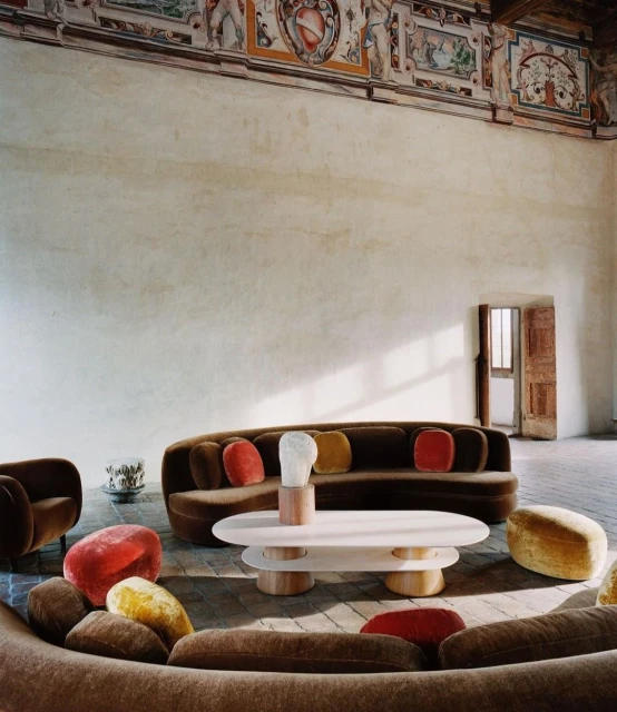 Interior view of a living room featuring a brown curved sofa with colorful pillows, a white coffee table, and artful decor accents.