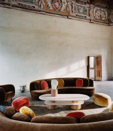 Interior view of a living room featuring a brown curved sofa with colorful pillows, a white coffee table, and artful decor accents.