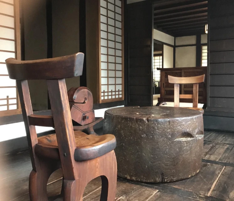 Interior view featuring a wooden chair and table in a traditional Japanese room with shoji screen windows and dark wood trim, creating a warm atmosphere.