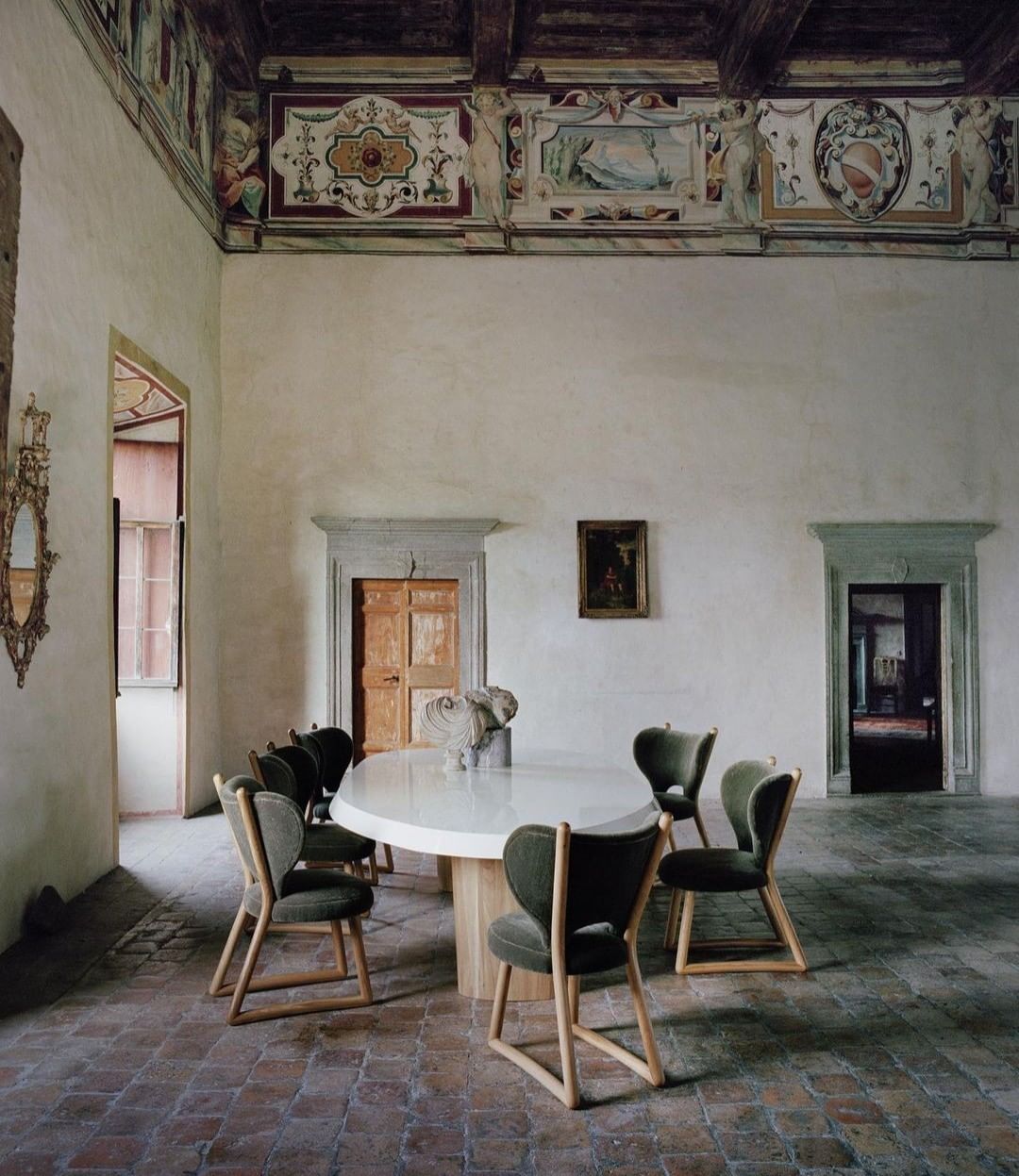 Interior photo of a dining room with white walls, arched doorways, tiled floors, and a wooden dining table with chairs. 