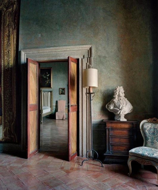 Interior view through open doorway with antique bust on a cabinet, chair, floor lamp, and tiled floor.