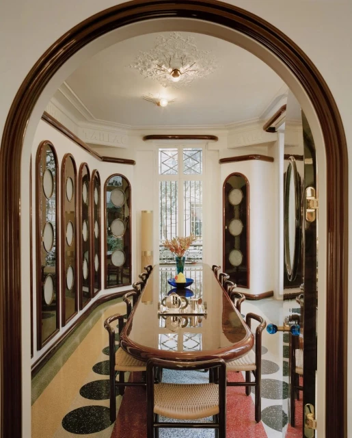 Interior view of a glossy dining room with an oval table, straw chairs, and arched doorways, creating a luxurious, modern design.