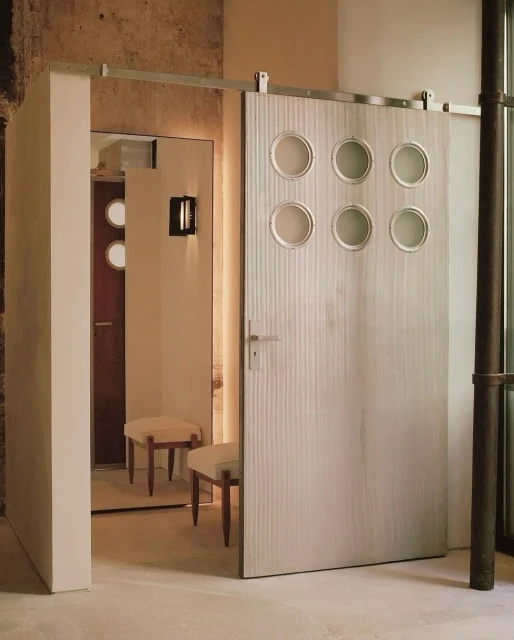 Interior view featuring a sliding barn door with round windows, beige stools, architectural details and neutral color palette.