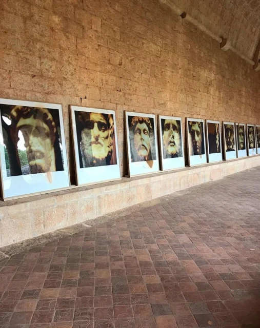 Exhibition of framed portraits with classical bust renderings adorns a brick-walled interior, arranged in a horizontal line, creating a gallery effect.