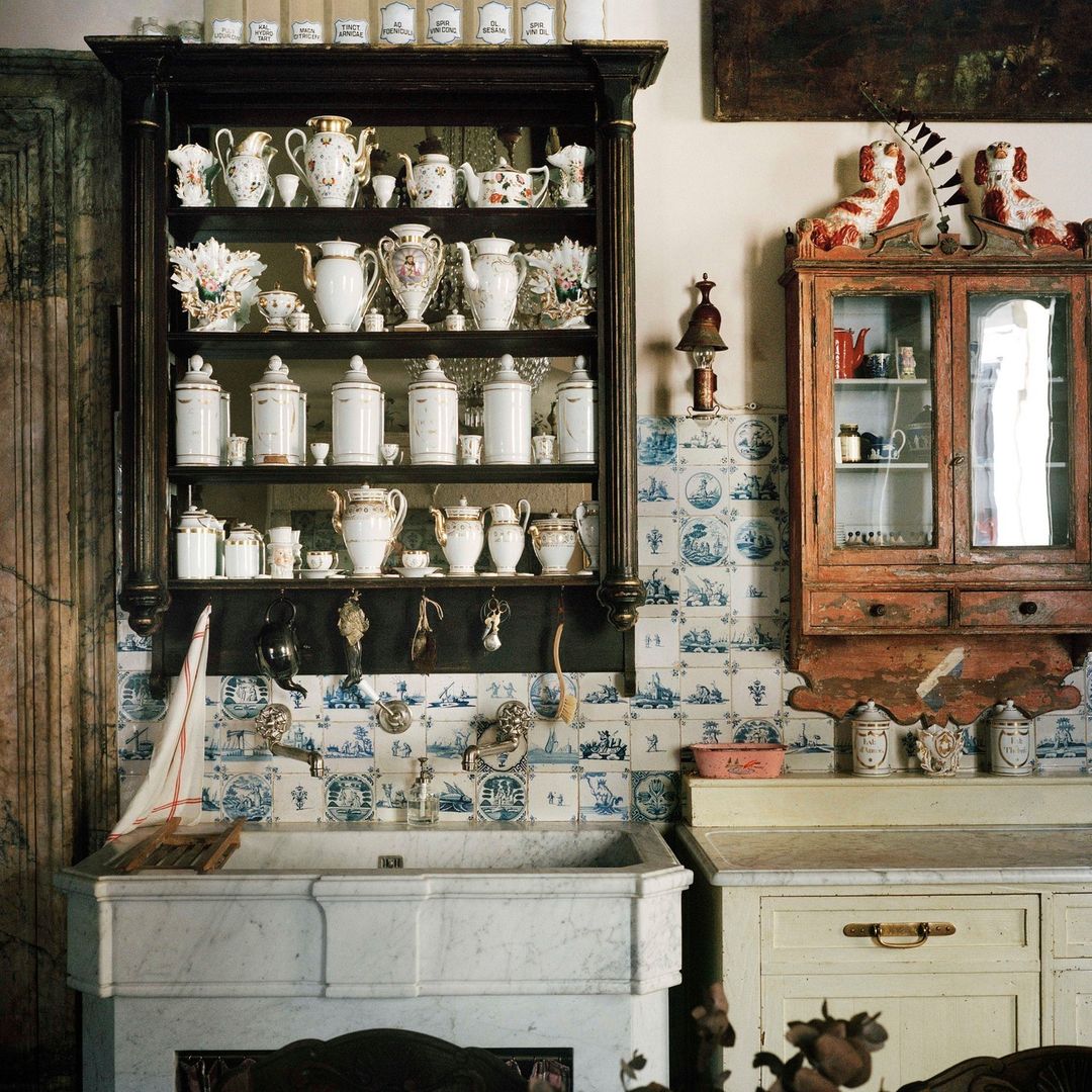 Vintage kitchen interior with antique cabinets, sink, white and blue tile, and dishware collection on display in a home.