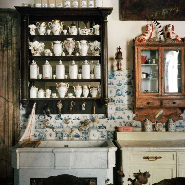 Vintage kitchen interior with antique cabinets, sink, white and blue tile, and dishware collection on display in a home.
