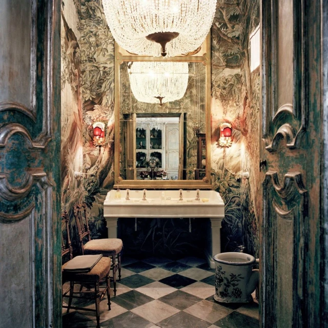 Ornate bathroom interior with checkerboard floor, wallpaper featuring forest scenes, antique wash basin, and decorative chandelier.