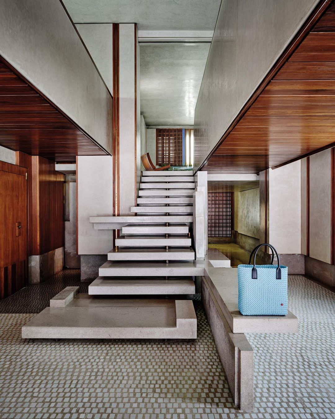 Interior view of a modern home showcasing a turquoise woven tote bag, concrete stairs, and wood paneling.