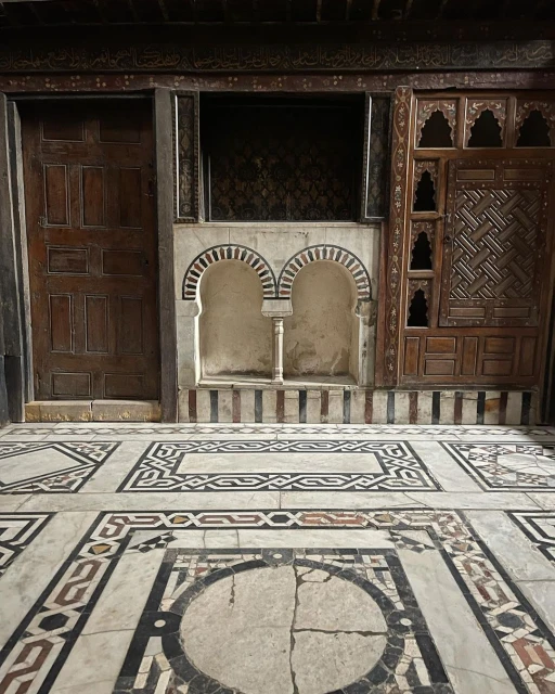 Interior view of a room with a decorative marble tile floor, an arched niche, and wood paneling, showcasing architectural details.