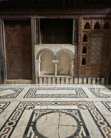 Interior view of a room with a decorative marble tile floor, an arched niche, and wood paneling, showcasing architectural details.