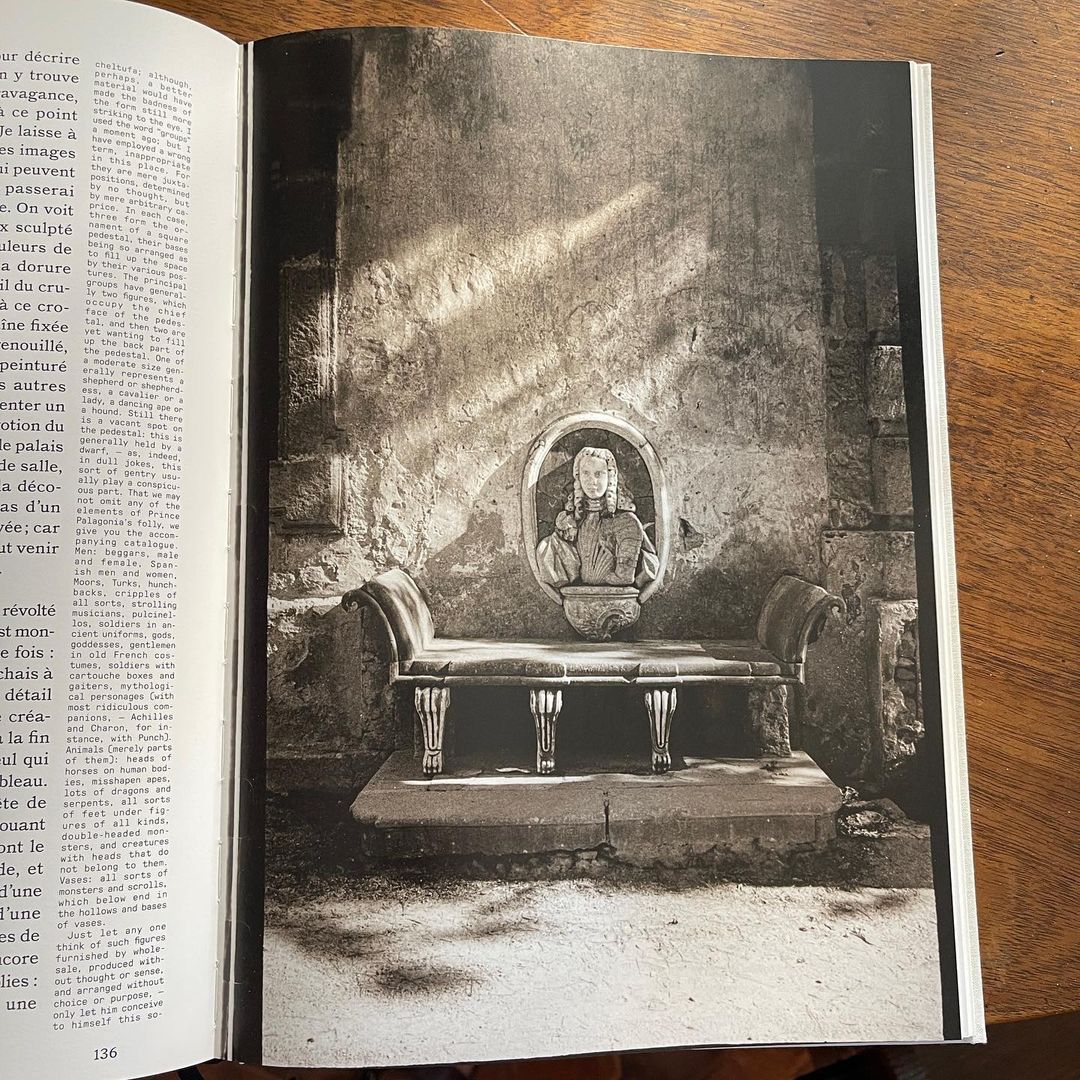 Monochrome photograph inside an open book features a sculptural bust on a bench against a textured wall with light streaks.
