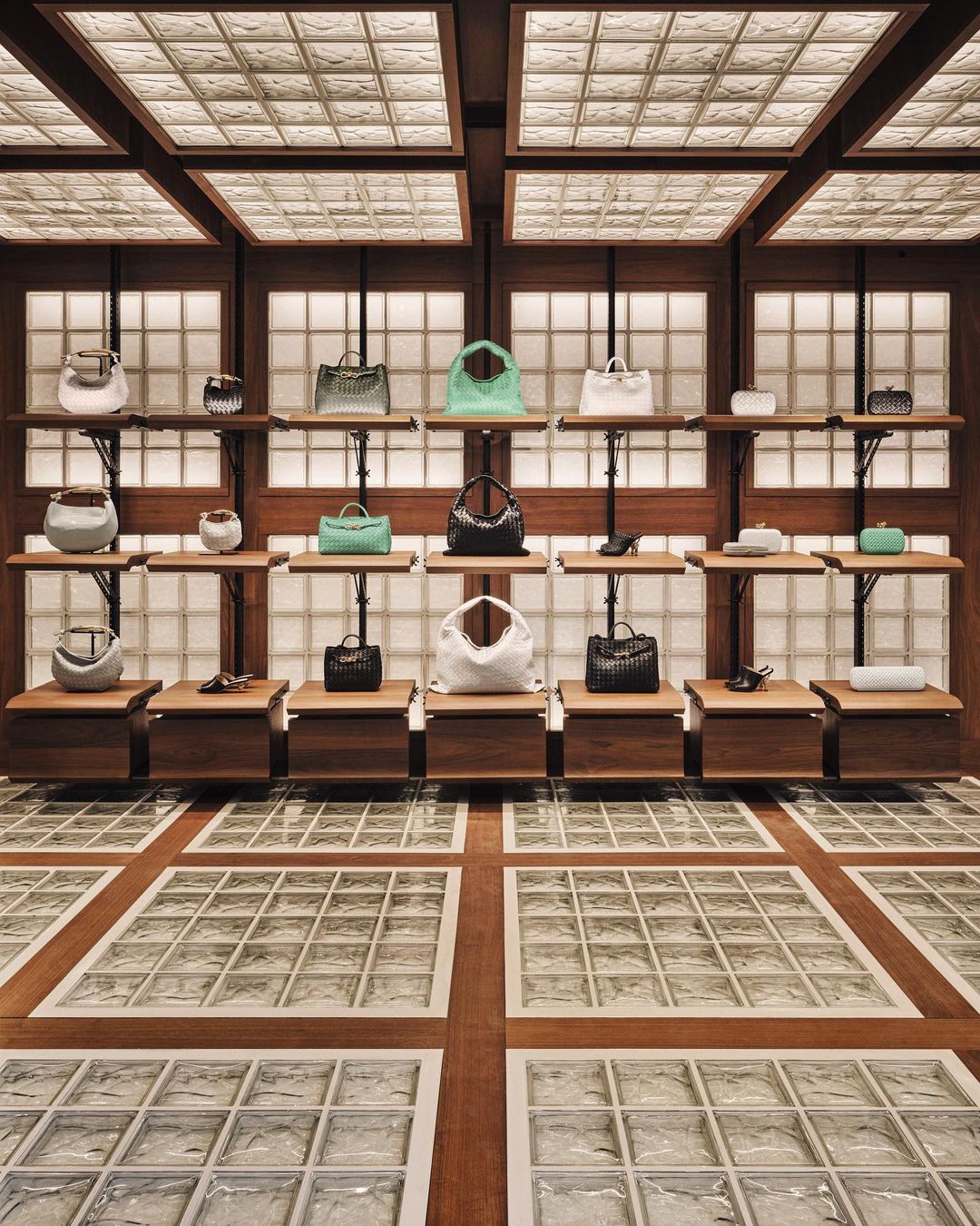 Luxury handbag display in a fashion boutique showcasing various styles and colors on wooden shelves against a textured wall.