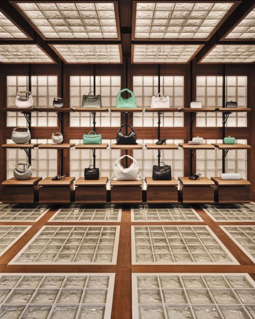 Luxury handbag display in a fashion boutique showcasing various styles and colors on wooden shelves against a textured wall.