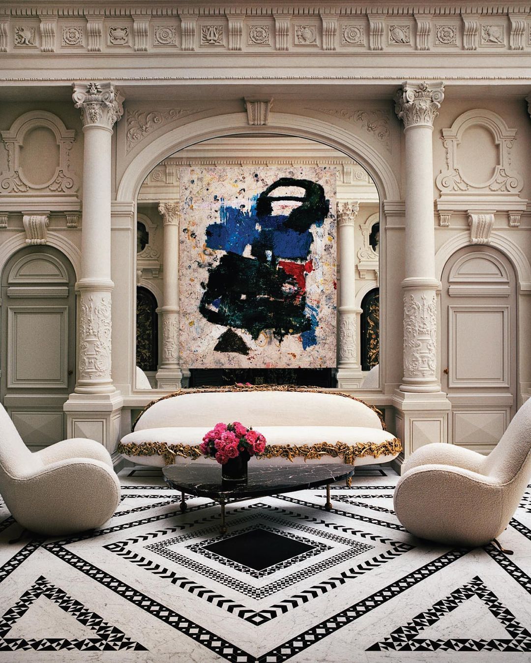 Elegant interior featuring a white sofa with gold trim, two armchairs, an abstract painting, and a black-and-white geometric patterned floor.