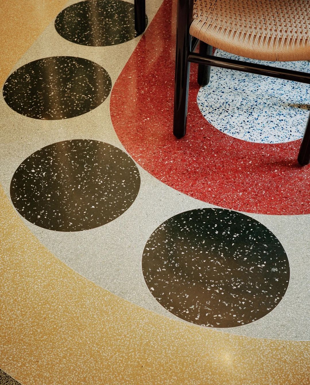 Close-up of a floor with a terrazzo-style surface featuring embedded stones and geometric shapes, alongside a portion of a chair.