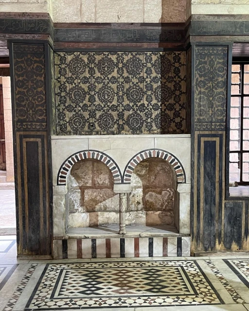 Ornate interior featuring tiled walls and floors, with decorative arches and patterns in beige, black, and brown tones.