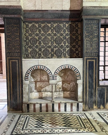 Ornate interior featuring tiled walls and floors, with decorative arches and patterns in beige, black, and brown tones.