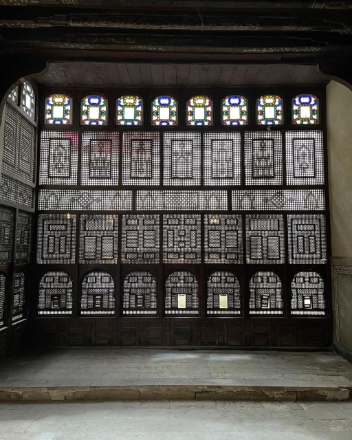 Intricate wooden lattice screen with geometric patterns and stained-glass windows, creating a play of light and shadow in the architecture.
