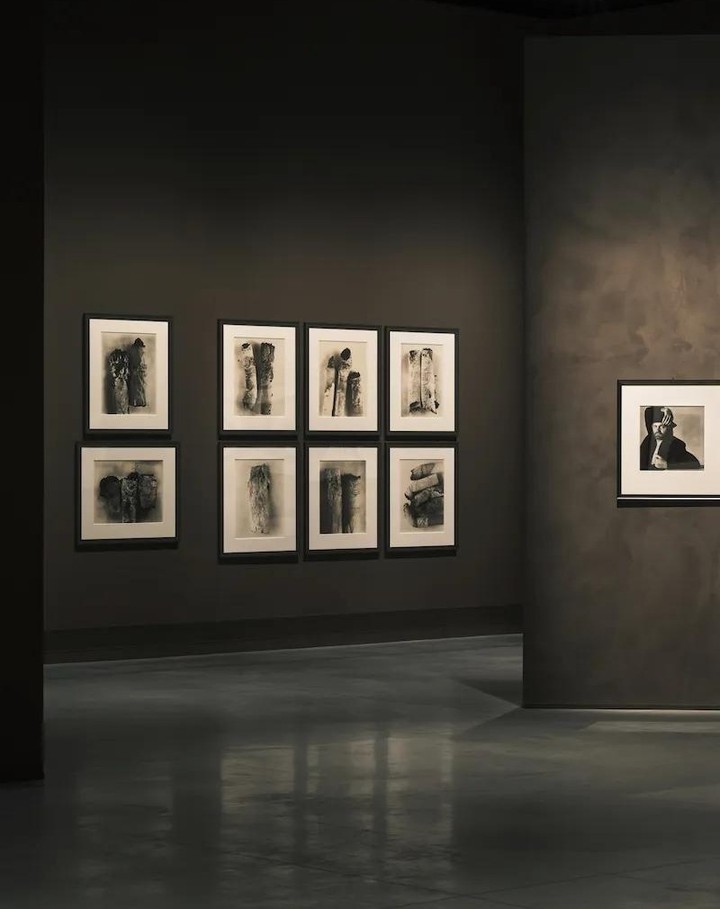 Art gallery features black-and-white abstract artworks displayed on dark gray walls, with a polished dark gray floor and neutral lighting.