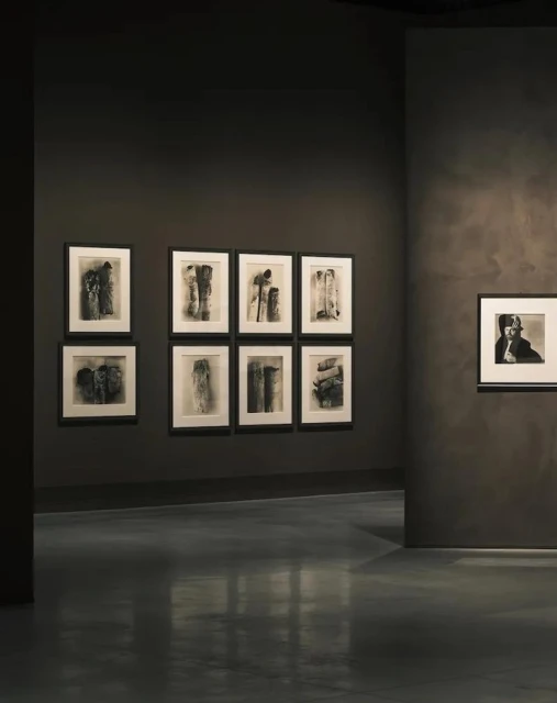 Art gallery features black-and-white abstract artworks displayed on dark gray walls, with a polished dark gray floor and neutral lighting.