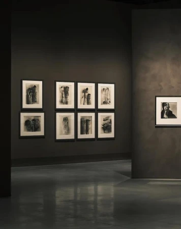 Art gallery features black-and-white abstract artworks displayed on dark gray walls, with a polished dark gray floor and neutral lighting.
