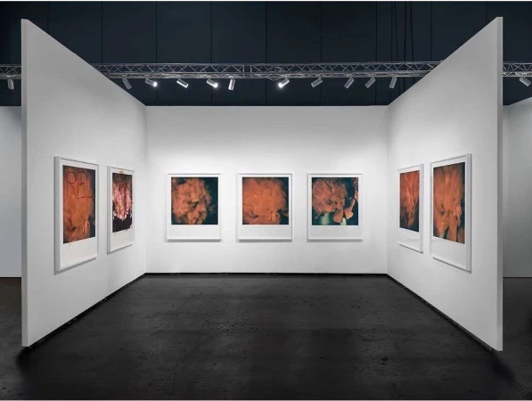 Interior view of an art gallery with framed photographs hanging on white walls, featuring black flooring and track lighting.
