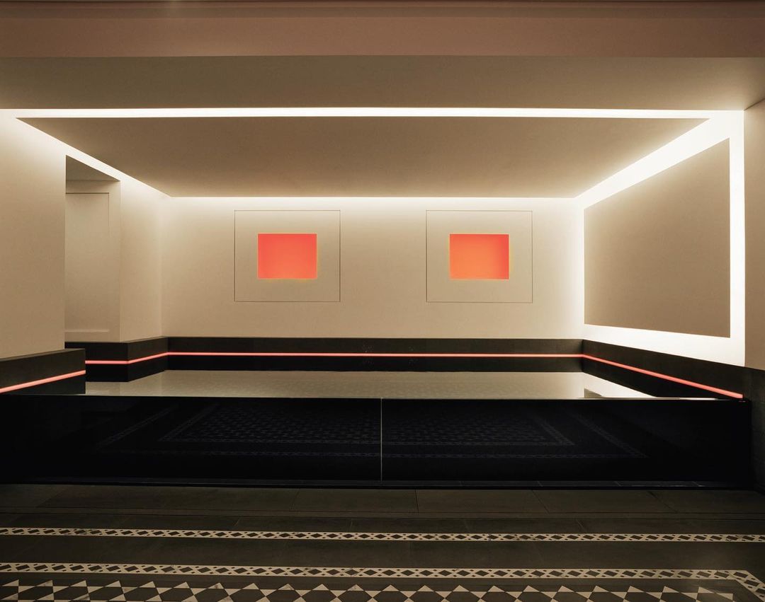 Modern interior features orange square artwork on white walls, highlighted by linear LED lighting, and reflective black surfaces.