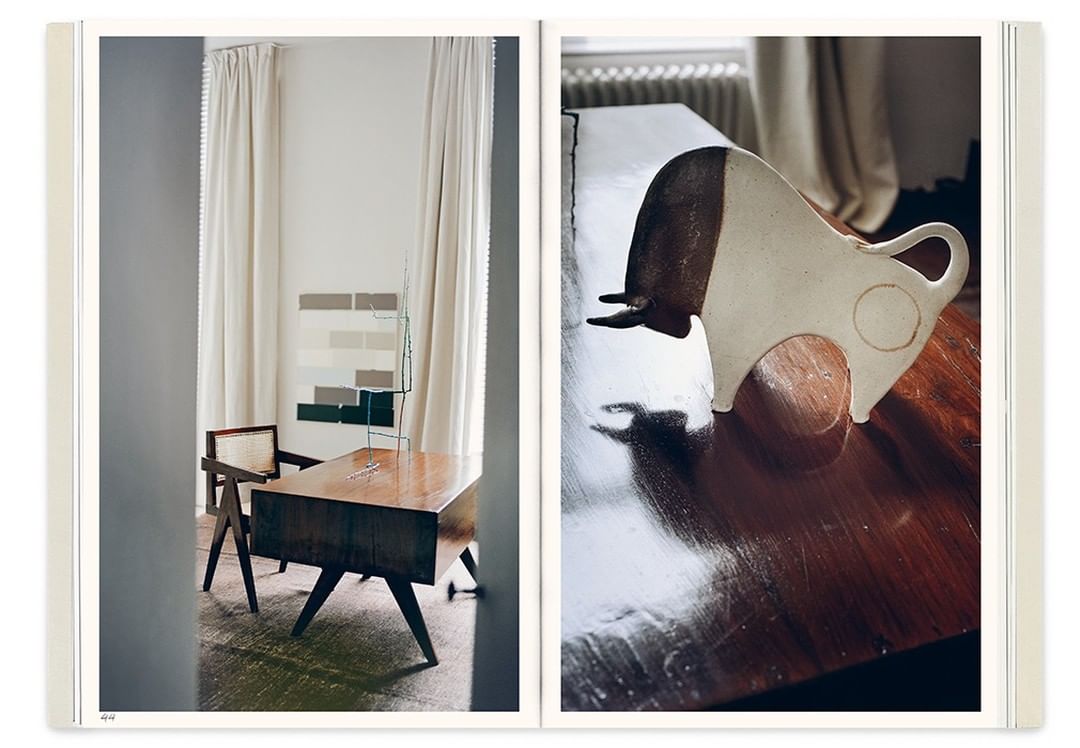 Still life featuring a ceramic bull sculpture and a modern wooden desk in an interior with white curtains and neutral-tone wall art.
