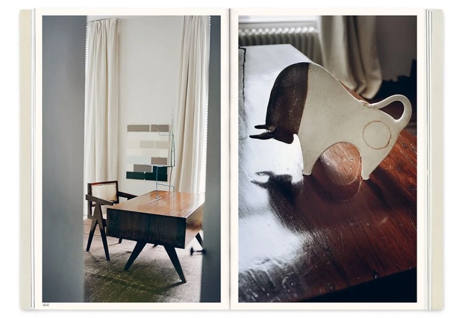 Still life featuring a ceramic bull sculpture and a modern wooden desk in an interior with white curtains and neutral-tone wall art.