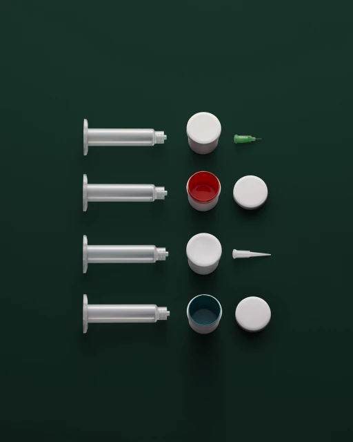 Overhead shot of four syringes, open containers with colorful liquid, and lids on a dark green background, shot in a studio.