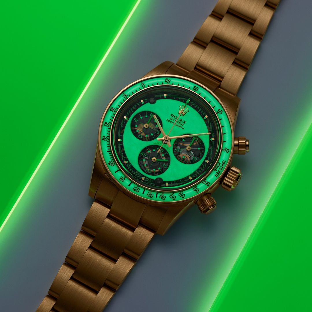 Gold Rolex Oyster Cosmograph Daytona with luminous green dial and hands in a studio setting with green neon lighting.