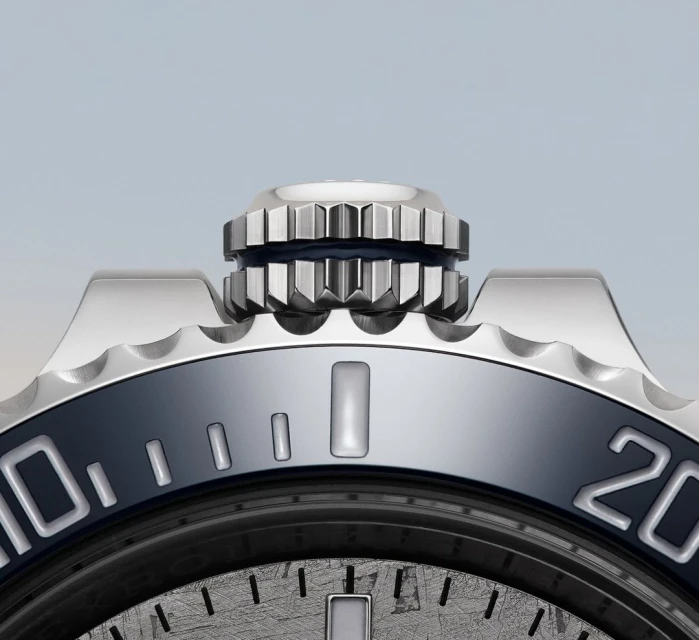Close-up of a luxury wristwatch featuring a silver-tone metal case with a ridged bezel and a dark dial with raised indices.