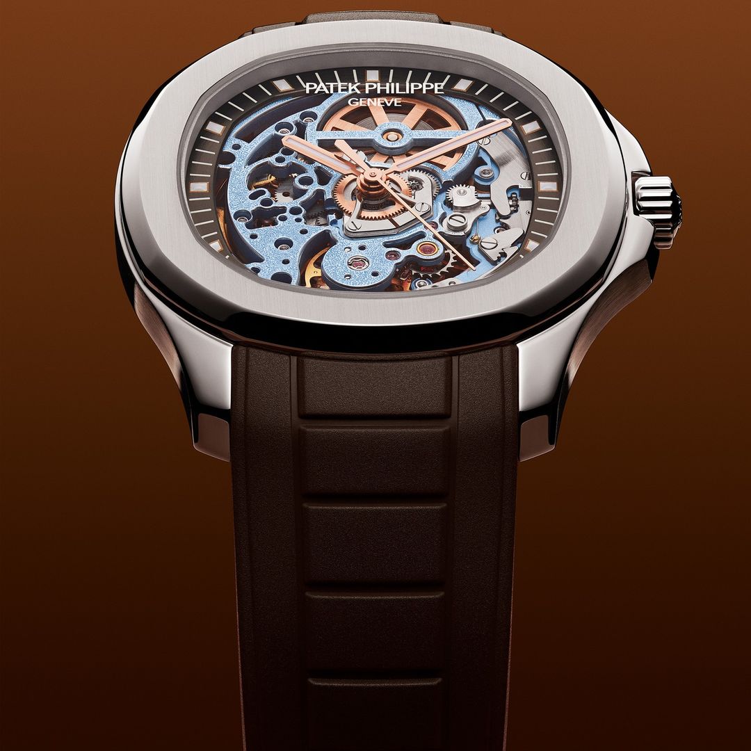 Close-up of a luxury Patek Philippe wristwatch featuring a skeleton dial and a brown rubber strap, set against a brown gradient background.