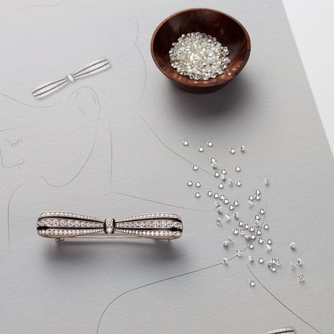 Bow-shaped brooch with diamond embellishments on a light grey surface with scattered diamonds and a small bowl of diamonds.