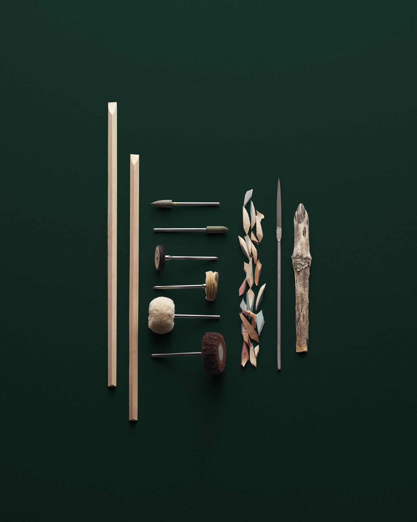 Still life of wood carving tools including rods, files, and carving pieces arranged on a dark green surface in a studio setting.