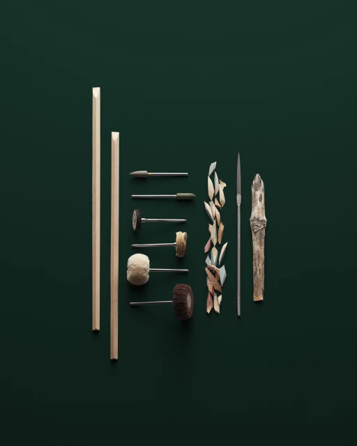 Still life of wood carving tools including rods, files, and carving pieces arranged on a dark green surface in a studio setting.