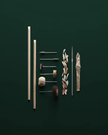 Still life of wood carving tools including rods, files, and carving pieces arranged on a dark green surface in a studio setting.