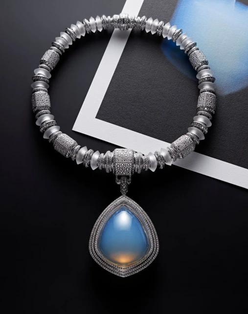 Necklace featuring a teardrop-shaped blue opal pendant and a graduated beaded chain with silver and frosted accents against a dark background.
