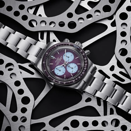 A close-up studio shot showcases a silver wristwatch with a purple face, encircled by cut metal, blending luxury with industrial textures.