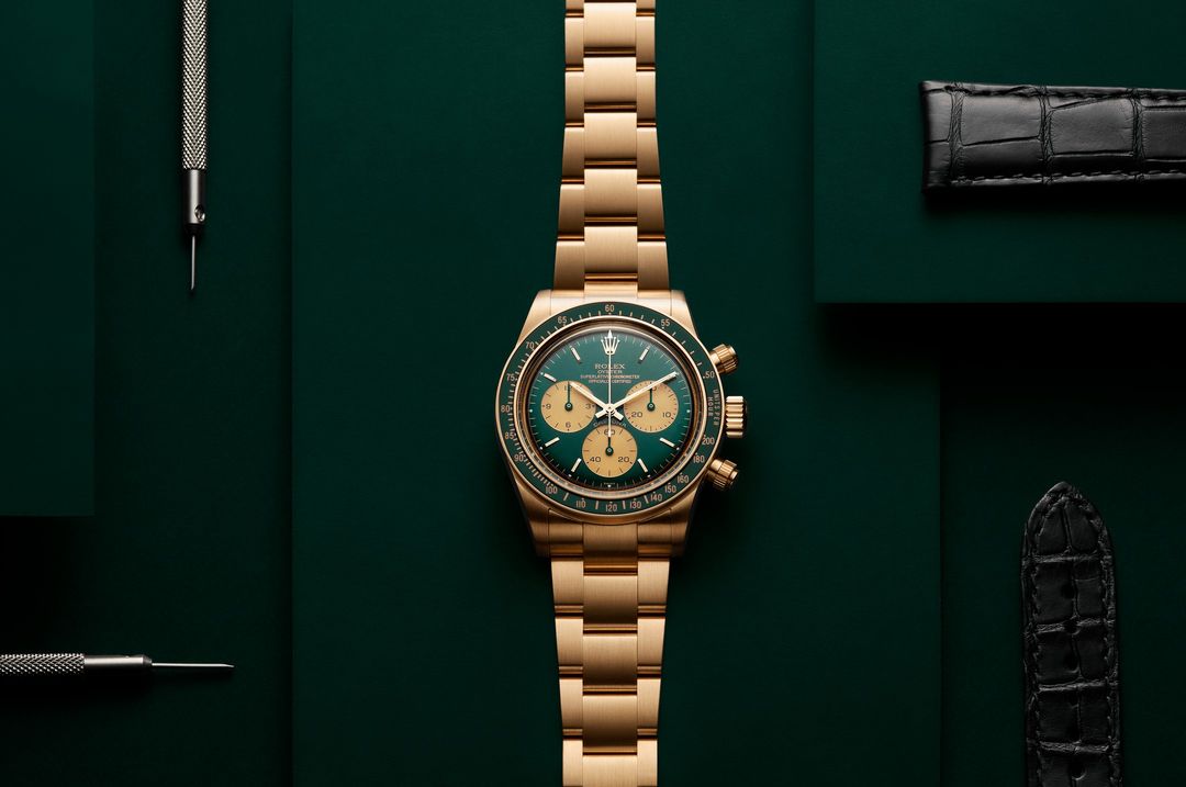 Luxury gold wristwatch with green dial and various watch straps and tools on a dark green backdrop. Timepiece and horology aesthetic.